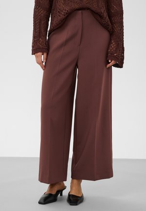 Femme portant un pantalon marron taille haute à jambes larges, des mules noires à talons et un pull en maille marron foncé à manches longues.