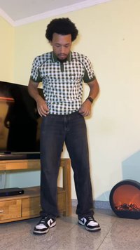 Zeleni in beli karirani polo majica, v kombinaciji s temno jeans hlačami in črno-belimi teniskami. V ozadju je črn televizor.