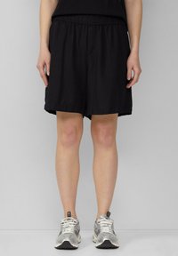 Zwarte shorts met elastische tailleband en een relaxed fit, met een subtiele textuur en een knielange snit. Gecombineerd met grijze sportschoenen.