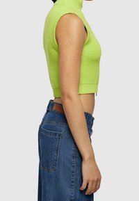 Top corto sin mangas de punto en un brillante verde lima, con cuello alto y textura acanalada, combinado con jeans de mezclilla de tiro alto.