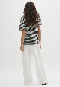 Black and white striped short-sleeve shirt paired with loose-fitting, white wide-leg trousers, featuring a soft texture and relaxed silhouette.