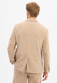 Beige Cordjacke mit Reverskragen, Rückenschlitz und leicht strukturiertem Stoff. Sie hat lange Ärmel und zwei Knöpfe an den Ärmelbündchen.