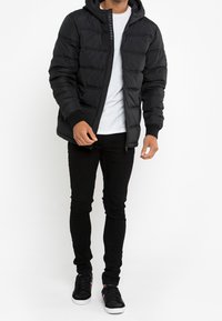 Czarna kurtka puchowa z kapturem, z zamkiem z przodu, ściągaczami na mankietach i pikowanym wzorem. Połączona z szarym t-shirtem i czarnymi dopasowanymi spodniami.