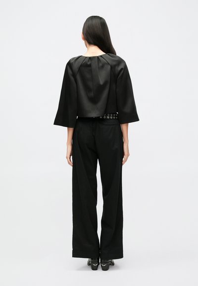 Schwarzes Satin-Cropped-Top mit dreiviertel Ärmeln und Falten-Detail am Rücken. Kombiniert mit hoch taillierten schwarzen Hosen mit weitem Bein und klobigen Schuhen mit Absatz.
