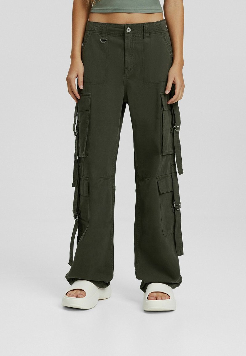 Pantalons cargo en vert olive, fabriqués dans un tissu résistant, dotés de plusieurs poches latérales, d'une coupe ample et d'accents en métal argenté.