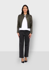 Olivově zelená kožená zkrácená bunda se dvěma zlatými knoflíky, nošena přes bílé tričko. V kombinaci s černými vysokými pasem džíny a černými špičatými botami.