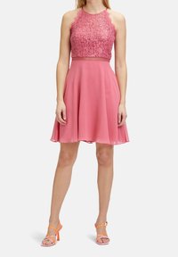 Sleeveless pink dress with lace bodice, fitted waist, and flared chiffon skirt. Paired with open-toe heels featuring coral straps.