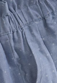 Ljusblått tyg med ett subtilt mönster av små, vita geometriska former. Samlade sömmar synliga längs kanten. Mjuk textur.