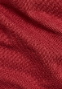 Röd texturerad tyg med ett vävt mönster, som har en mjuk, något glansig yta och en mild fall. Djup och dimension är synliga.