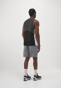 Camiseta de tirantes atlética en blanco y negro, pantalones cortos de malla grises y zapatillas negras. Presenta bloqueos de color verticales y tela texturizada. Calcetines blancos visibles.