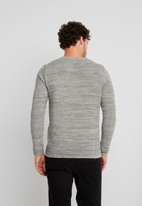 Gray long-sleeve knit sweater with a textured striped pattern, rounded neckline, and fitted sleeves, worn with black pants.