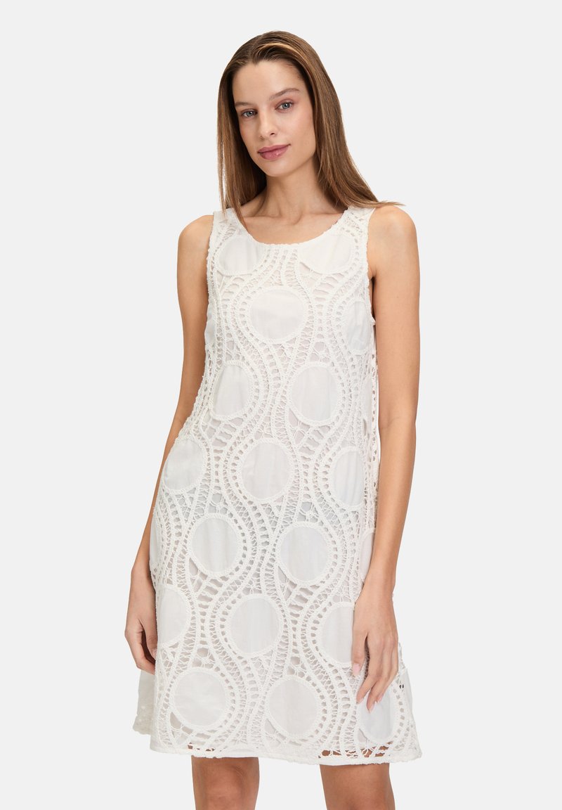 Weißes ärmelloses Kleid aus Spitze mit runden Ausschnitten und gewellten Linienmustern. Lockerer, knielanger Schnitt.