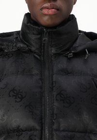 Melna pūkaina jaka ar augstu apkakli, rāvējslēdzēja priekšpusi un smalku logo rakstu. Materiāls izskatās gluds ar spīdīgu apdari.