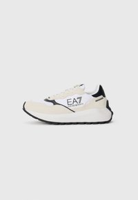 White and cream sneaker with black accents, suede and mesh materials, rounded toe, thick sole, and logo detailing on the side.
