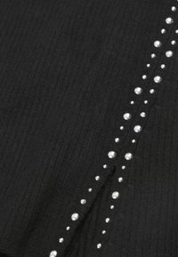 Tissu côtelé noir avec une ligne verticale de perles argentées sur un côté, créant un détail texturé et décoratif.