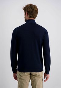 Marineblauwe gebreide trui met een hoge kraag en een getailleerd ontwerp. Beschikt over lange mouwen en een gladde textuur. Gekocht met lichte kaki broek.