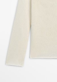 Manica di maglione lavorato a maglia a manica lunga color panna e bordo inferiore su sfondo bianco, che mostra la trama e il motivo delle maglie.