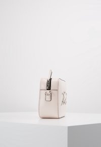 Mała, prostokątna torba z jasnoróżowej ekoskóry z srebrnym zamkiem błyskawicznym i metalowymi elementami, z wyraźnym wytłoczonym logo z przodu.