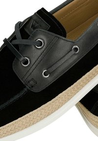 Schwarze Wildleder- und Lederschuhe mit einer geflochtenen beigen Mittelsohle, ausgestattet mit silbernen Ösen, schwarzen Schnürsenkeln und einem glatten Innenfutter.
