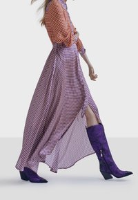 Vestido largo y fluido con un patrón de espigado rojo y púrpura; combinado con botas altas moradas con textura floral y detalle de cremallera.