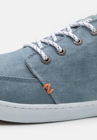 Helles blaues Canvas-Sneaker mit weißen Schnürsenkeln, Metallösen, orangen Nähten und strukturiertem Gummisohle.