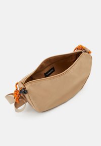 Borsa di tessuto beige con una zip aperta, che mostra una tracolla annodata arancione e nera. Texture liscia, forma rettangolare compatta.