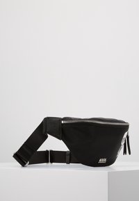 Zwarte nylon heuptas met een gebogen vorm, zilveren rits, reliëflogo en verstelbare schouderband, met een accentgraphic aan de voorkant.