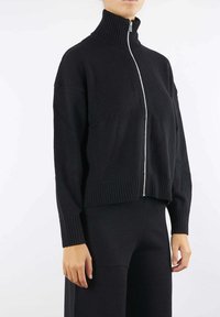 Maglione a maglia nera con colletto alto a coste, zip frontale completa e orlo a coste. Design semplice, maniche lunghe e vestibilità comoda.