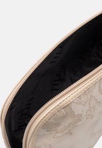 Bustina beige con cerniera e motivo astratto testurizzato. L'interno è foderato in tessuto nero, con il nome del marchio ripetuto in stampa.