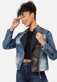 Jeansjacke mit einem Reißverschluss vorne, einem gefütterten inneren Futter mit geometrischen Mustern und einem Kragen mit Druckknöpfen. Ausgewaschene blaue Farbe.