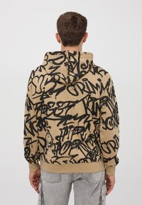 Felpa con cappuccio di colore tan, caratterizzata da motivi di testo in stile graffiti neri, polsini e orlo a coste, con cappuccio regolabile e vestibilità morbida.
