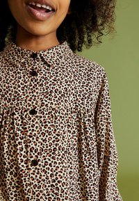 Leopardi-kuvioinen paita, jossa on kaulus, mustat napit ja ryyttäys. Sujuva kangas, jossa on vaaleanbeigejä, ruskeita ja mustia sävyjä.