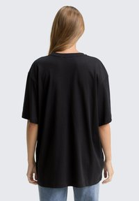Zwarte oversized t-shirt met korte mouwen en een ronde hals. Gemaakt van zachte stof, met een gladde textuur en een ontspannen pasvorm.
