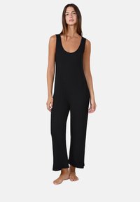 Mono negro con acanalado, escote de barco, diseño sin mangas, piernas amplias y un corte relajado. Fabricado en un material suave y elástico.