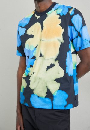 T-shirt à manches courtes en tissu avec une base noire ornée de grands motifs floraux jaunes, bleus et verts. Encolure ronde, coupe décontractée.