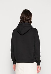 Una persona con el cabello oscuro a la altura de los hombros, vista desde detrás, lleva una sudadera negra combinada con una falda de color claro.