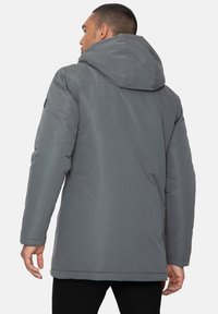 Graue gepolsterte Jacke mit Kapuze, die eine glatte Textur, lange Ärmel und einen mittellangen Schnitt aufweist. Auffällige Details sind die genähten Nähte und das Logo.