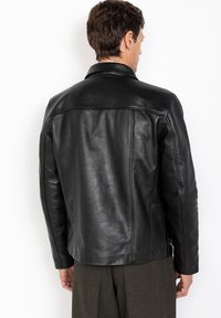 Veste en cuir noir à texture lisse, col standard et épaules structurées. Présente des détails de coutures et une coupe ajustée.
