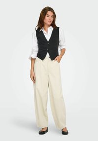 Gilet en laine gris foncé avec un design ajusté, boutons sur le devant, chemise blanche à col en dessous, associé à un pantalon large taille haute beige et des ballerines noires.