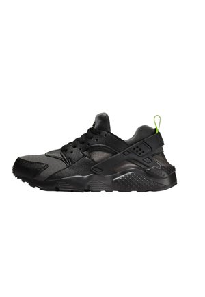 Zapatilla deportiva negra que presenta una mezcla de materiales texturizados, una suela de goma y un acento en verde neón en la lengua del talón.