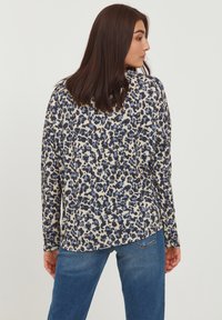 Langarmshirt in cremfarbener Basis mit blauem und schwarzem Leopardenmuster, mit einem lockeren Schnitt und rundem Ausschnitt, getragen mit blauen Jeans.