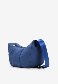 Bolso de hombro de nylon azul marino con forma curva, correa azul ajustable y un bolsillo delantero con cremallera. Textura suave con costuras sutiles.