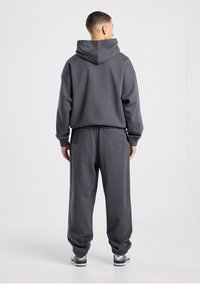 Grijze capuchontrui en bijpassende joggingbroek gemaakt van zachte stof. Losse pasvorm, elastische manchetten aan de broek en subtiele stikdetails.