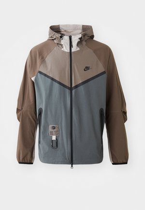 Chaqueta de Nike con un diseño en bloques de color en gris y marrón, con capucha ajustable, cierre de cremallera y bolsillos laterales. Detalles de tejido texturizado.