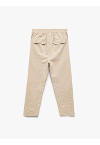 Pantalones ligeros en color beige con una textura arrugada, cintura elástica y dos bolsillos traseros. Diseño de pierna recta.