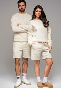 Krémově barevné unisex mikiny a kraťasy z měkké látky; mikina s žebrovanými manžetami, kraťasy se stahovací šňůrkou a kapsami.