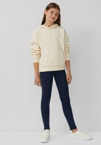 Crème-kleurige hoodie met een voorzak, gecombineerd met marineblauwe leggings en witte sneakers. Glad textuur, relaxte pasvorm en eenvoudig ontwerp.