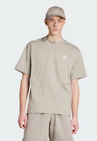 Beżowy T-shirt z okrągłym dekoltem, wykonany z miękkiego materiału, posiadający krótkie rękawy i subtelne logo w diagonalne paski na piersi. W komplecie z beżowymi szortami.