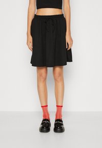 Svart kjol med elastisk midja och dragsnodd. Utställd form, mjuk textur. Pairad med röda strumpor och svarta glänsande skor.