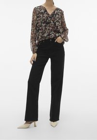 Blusa nera trasparente a fiori con scollo a V e maniche lunghe, abbinata a pantaloni neri a vita alta e gamba dritta, e décolleté crema con punta sottile.